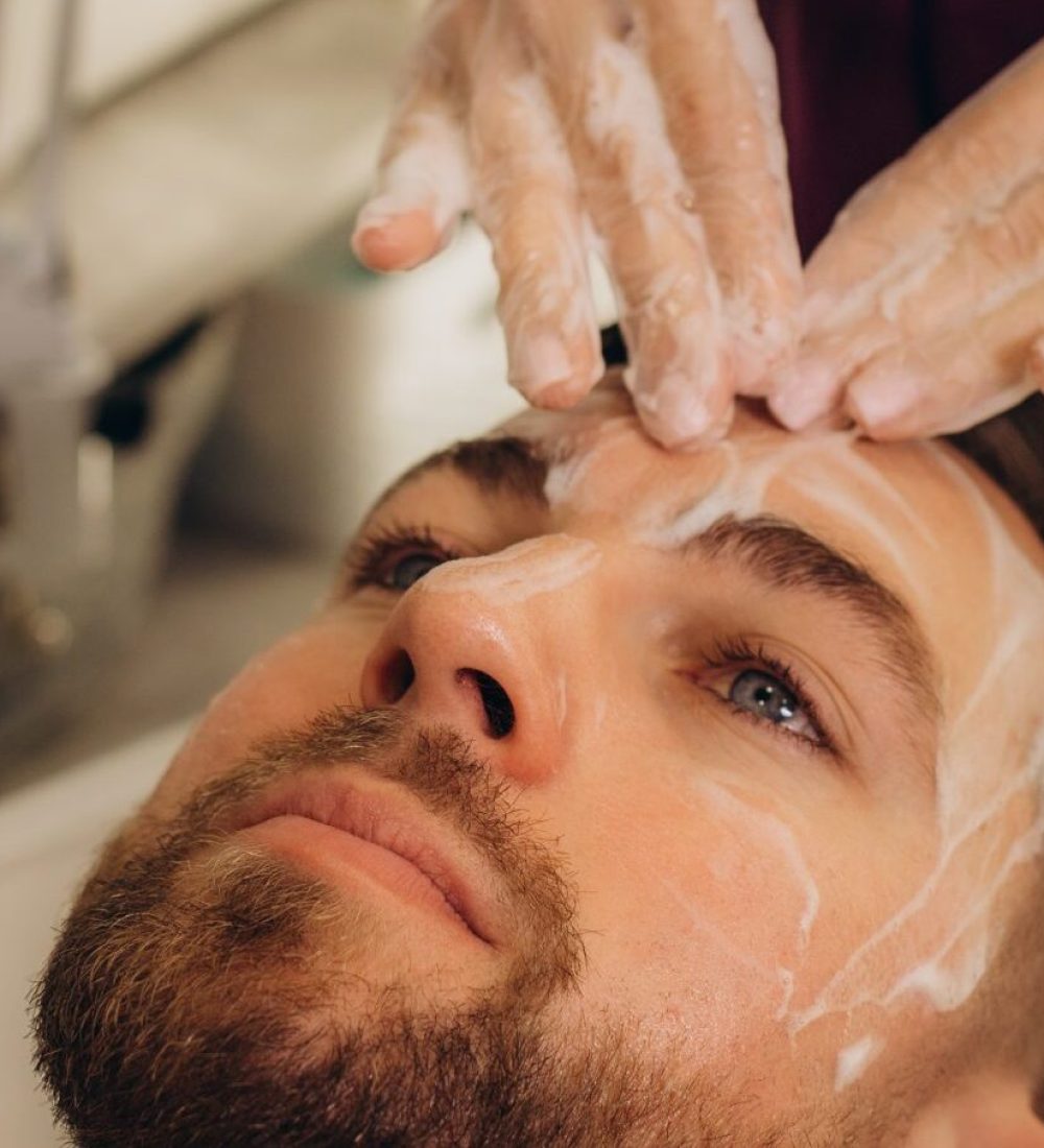 Cosmetologist applying mask on man's face in spa salon, top view. High quality photo